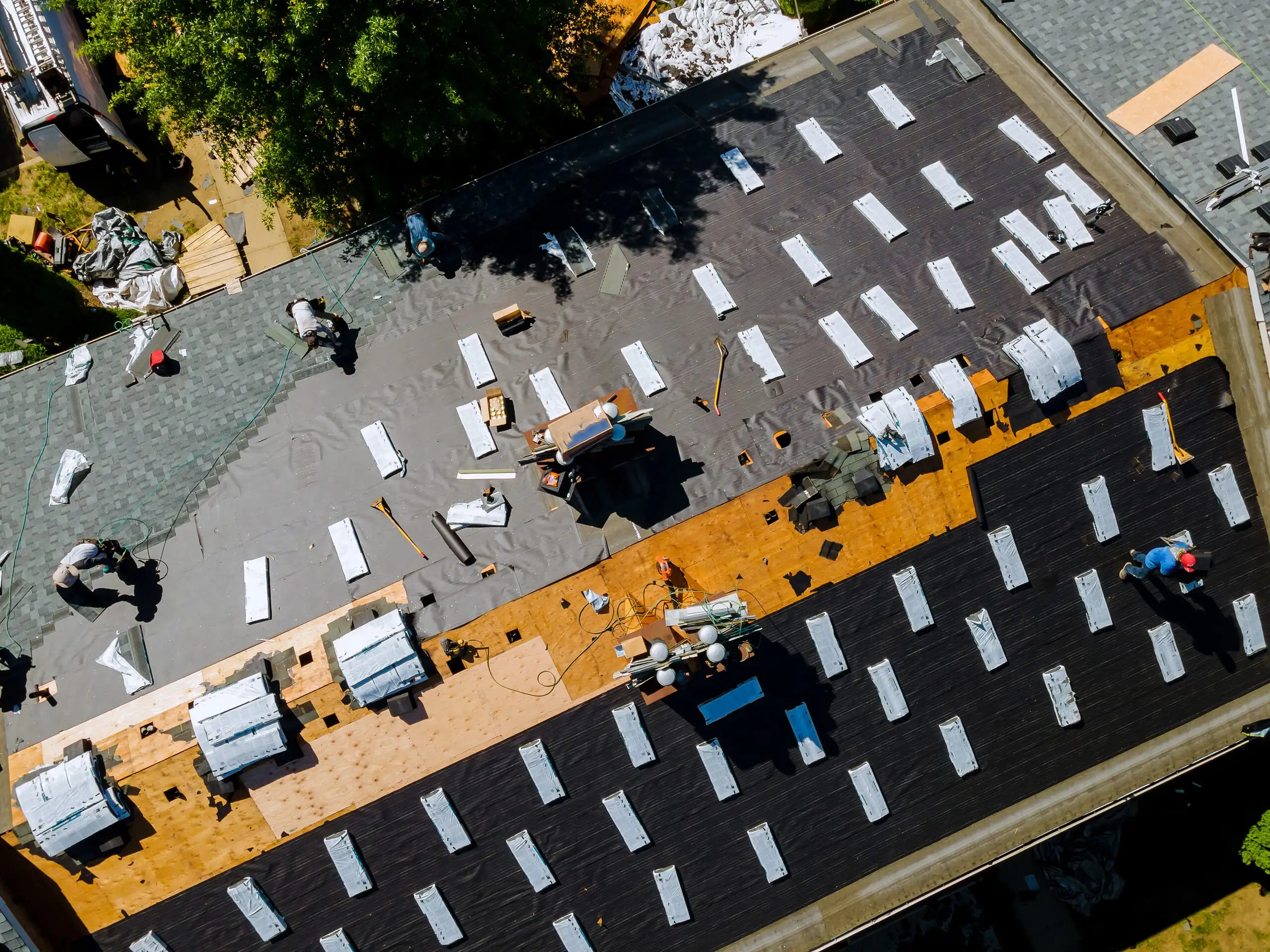 Aerial view of a roofing crew laying new underlayment and shingles over bare decking