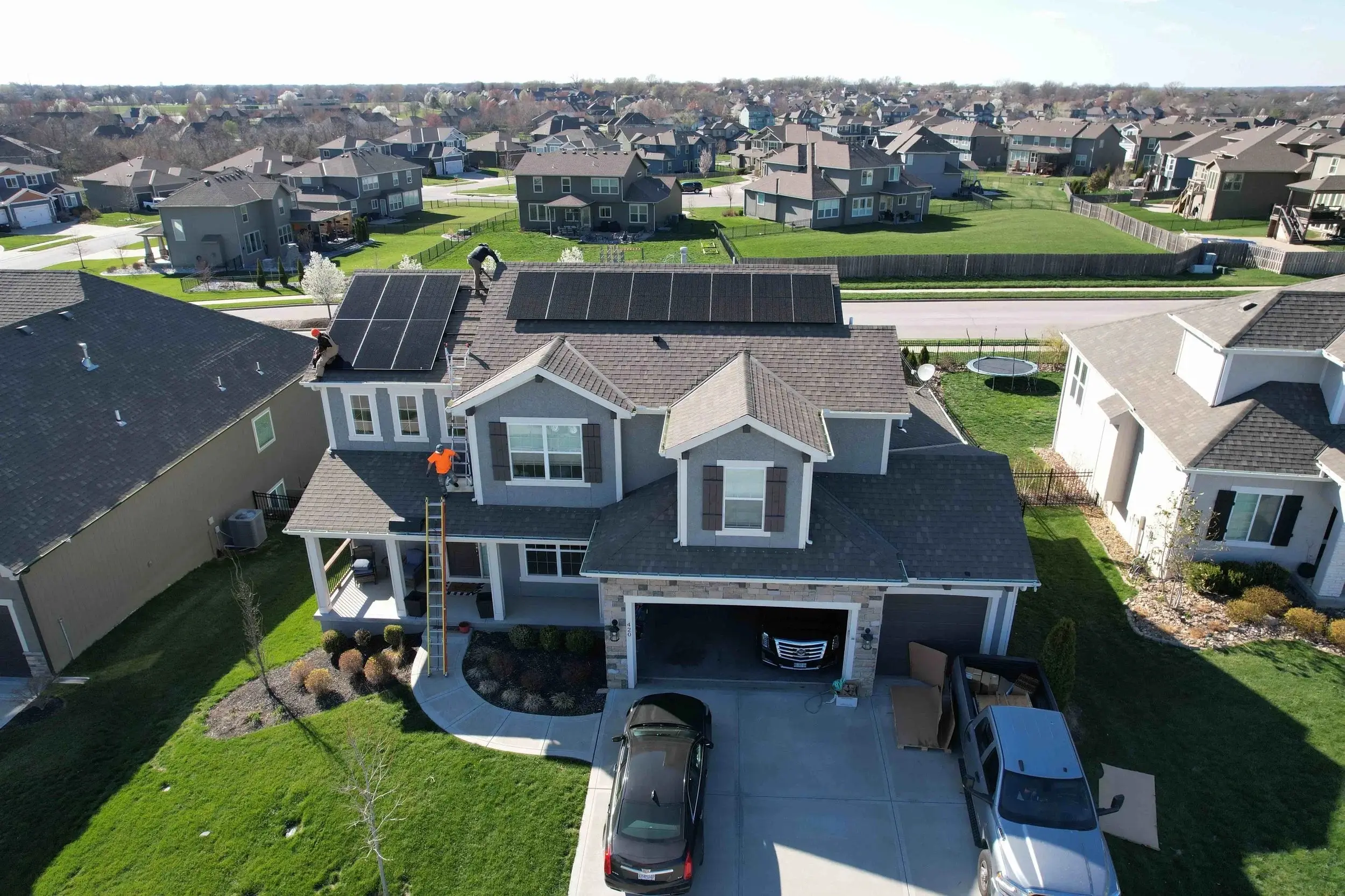 Drone view of a Helio Contracting crew member on a two-story shingle roof with solar panels